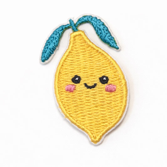 Bestickter Aufnäher in Form einer lächelnden Zitrone mit türkisfarbenen Blättern, rosa Wangen und schwarzen Augen auf weißem Hintergrund. Größe 4x2,5cm, zum Aufbügeln oder Aufnähen.