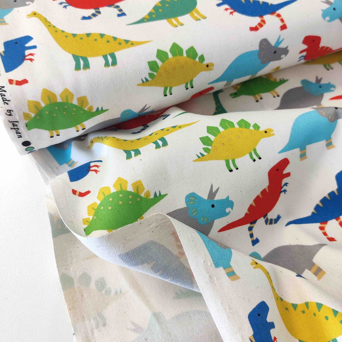 Japanischer Baumwollstoff von Sevenberry mit bunten Dinosauriern auf naturfarbenem Hintergrund.