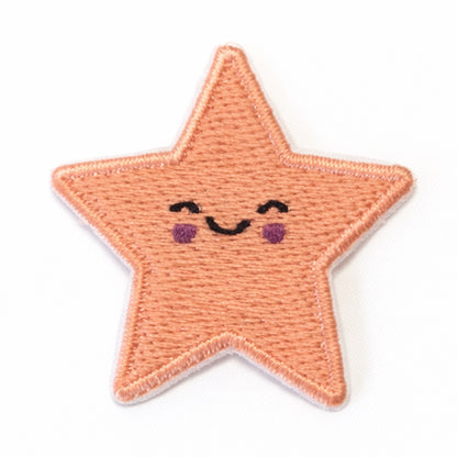 Bestickter Stern-Aufnäher in Apricot mit lächelndem Gesicht, geschlossenen Augen und roten Wangen. Größe 3,5x3,5cm, zum Aufbügeln oder Aufnähen.